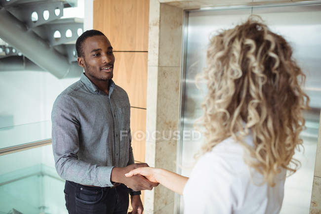 Ejecutivos de negocios estrechando manos cerca de ascensor en la oficina - foto de stock