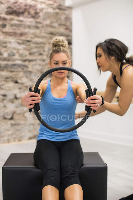 Entrenadora mujer que ayuda a la mujer con el ejercicio con anillo de pilates en el gimnasio - foto de stock