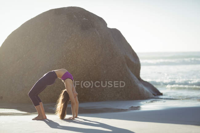 Красивая женщина выполняет упражнения на растяжку на пляже в солнечный день — стоковое фото