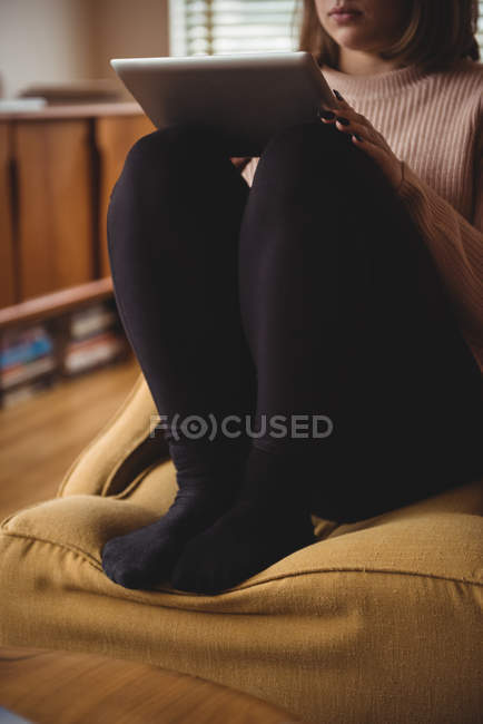 Femme assise sur une chaise en utilisant une tablette numérique dans le salon à la maison — Photo de stock