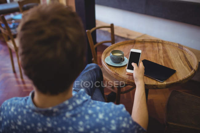 Вид ззаду людини, що використовує мобільний телефон за столом кафе — стокове фото
