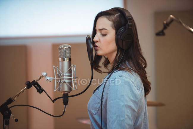 Woman singing on microphone in recording studio — Stock Photo