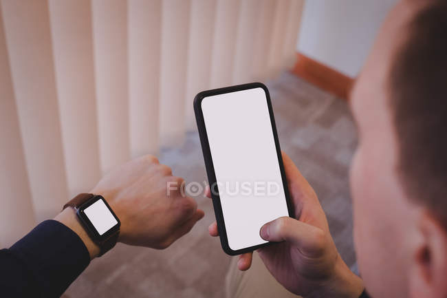 Male executive using mobile phone and checking time on wristwatch in office — Stock Photo