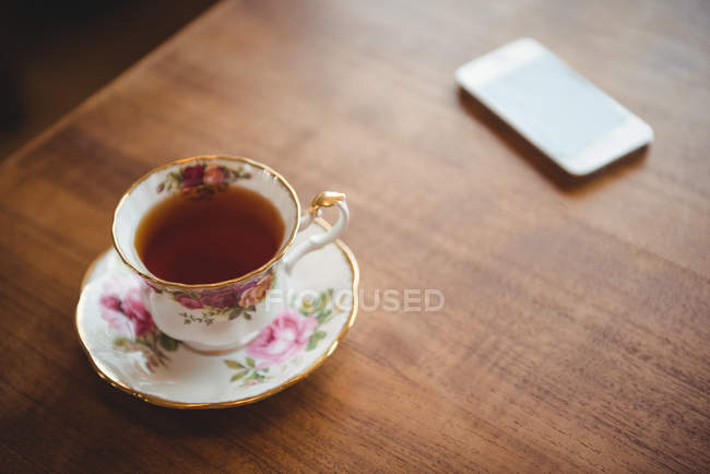 Xícara de chá e telefone celular em mesa de madeira em casa — Fotografia de Stock