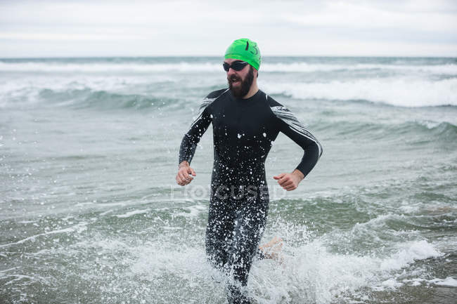 Спортсмен в мокром костюме бежит к пляжу — стоковое фото