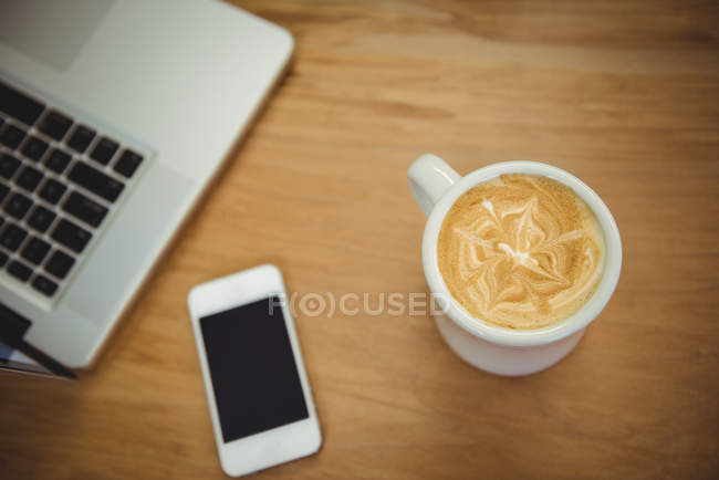 Gros plan de tasse à café, téléphone portable et ordinateur portable sur une table en bois — Photo de stock
