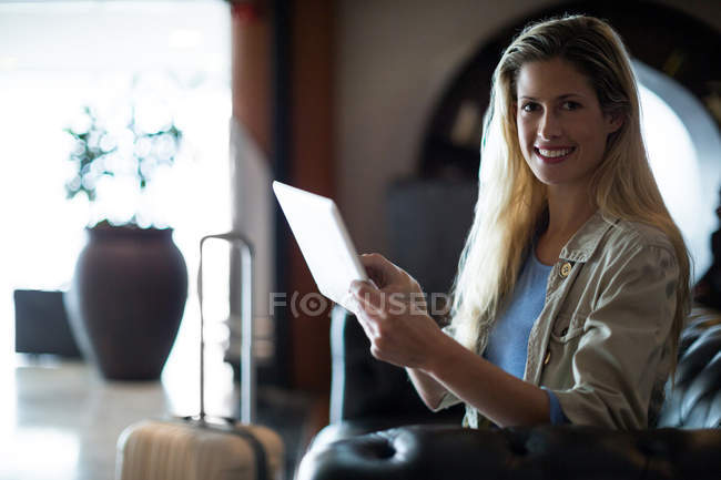 Retrato de mulher sorridente sentada no sofá com tablet digital na área de espera no terminal do aeroporto — Fotografia de Stock