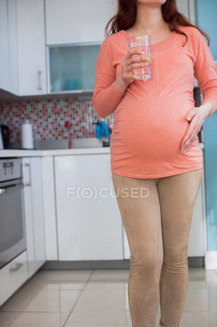 Середина вагітної жінки, що тримає склянку води на кухні вдома — стокове фото