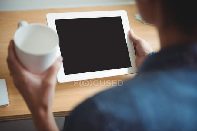 Business executive using digital tablet while having cup of coffee in office — Stock Photo