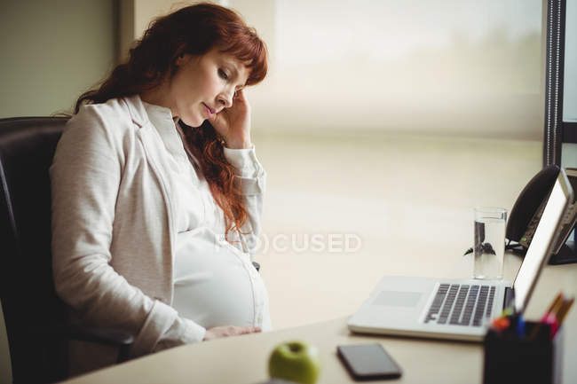 Femme enceinte réfléchie tenant ventre au bureau — Photo de stock