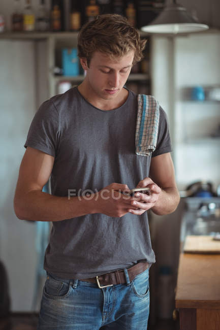 Homme debout dans la cuisine et utilisant le téléphone mobile — Photo de stock