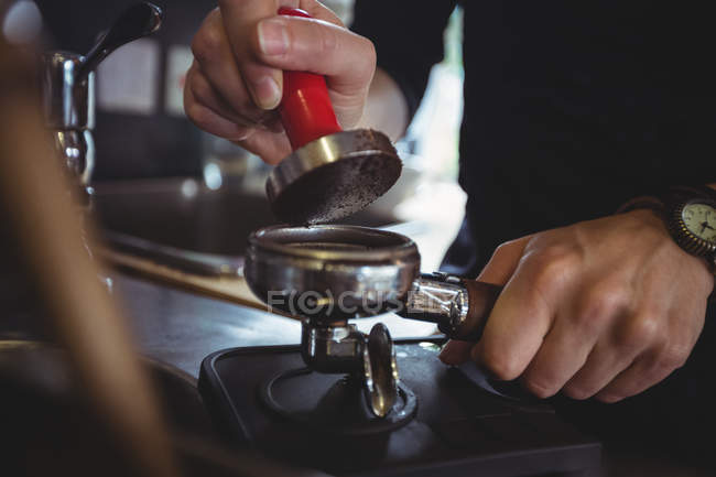 Gros plan de serveuse utilisant un tampon pour presser du café moulu dans un portable dans un café — Photo de stock