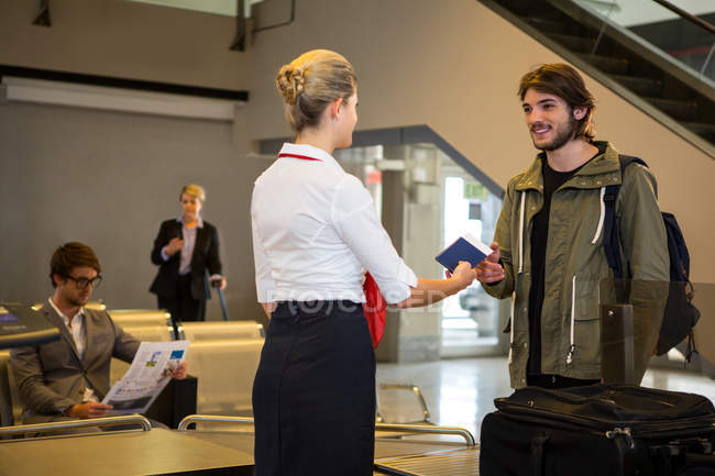 Hombre que interactúa con el personal del aeropuerto con el equipaje guardado en la cinta transportadora en la terminal del aeropuerto - foto de stock