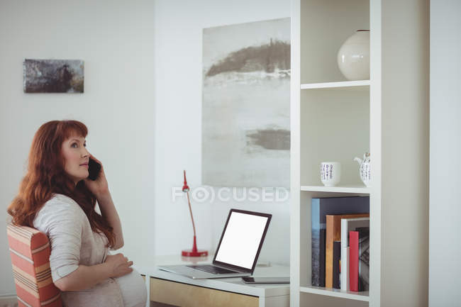 Pregnant woman talking on mobile phone in study room at home — Stock Photo