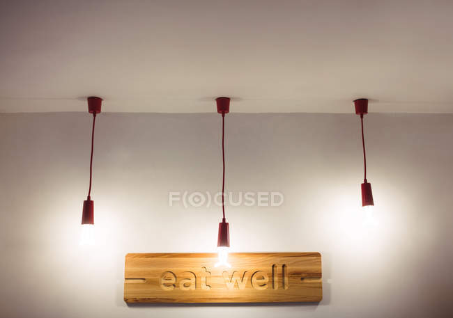Ceiling lights hanging in front of restaurant board with eat well signage — Stock Photo