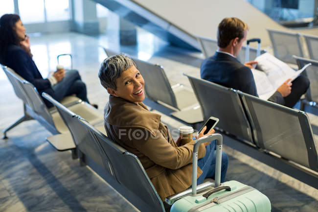 Commuter with coffee cup using mobile phone in waiting area at airport — Stock Photo