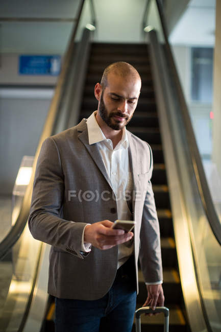 Empresário com bagagem usando telefone celular no aeroporto — Fotografia de Stock
