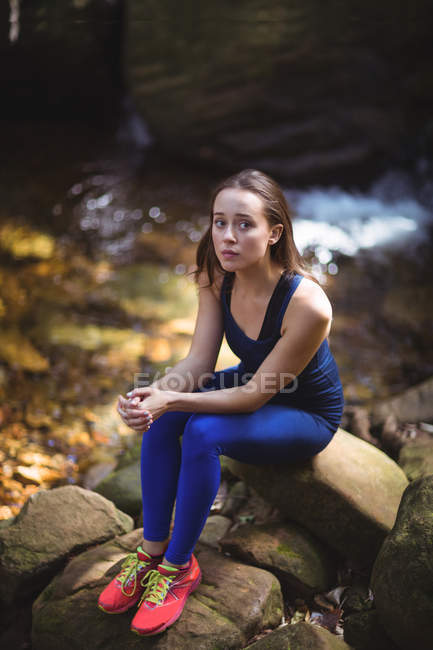 Mujer pensativa sentada en la roca en el bosque - foto de stock