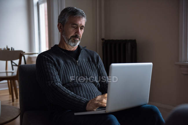 Мужчина сидит на диване и использует ноутбук дома — стоковое фото