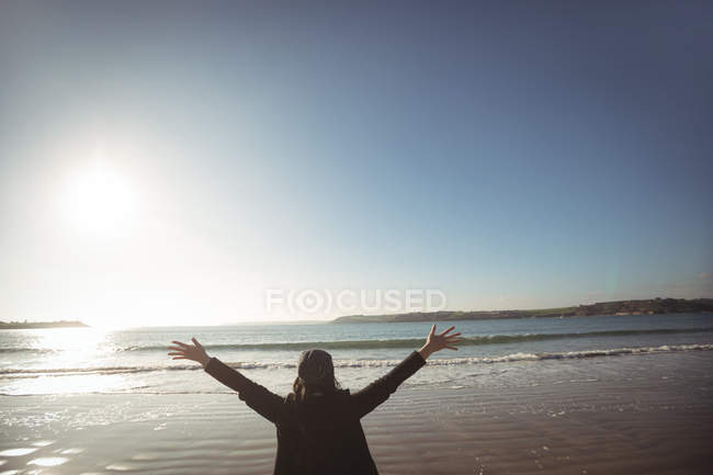 Rückansicht einer Frau, die tagsüber mit ausgestreckten Armen am Strand steht — Stockfoto