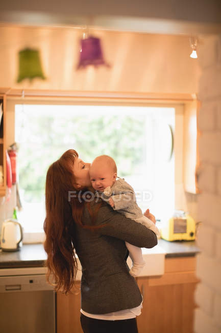 Ласковая мать держит младенца на кухне дома — стоковое фото