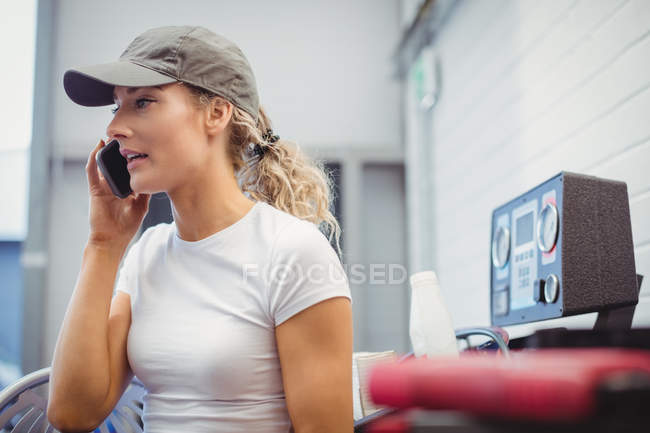 Feminino mecânico falando no telefone celular na garagem de reparação — Fotografia de Stock