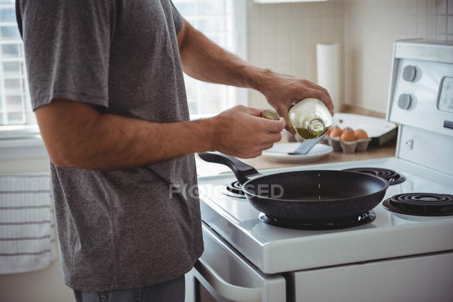 Mittelteil des Mannes gießt Olivenöl in die Pfanne in der Küche zu Hause — Stockfoto