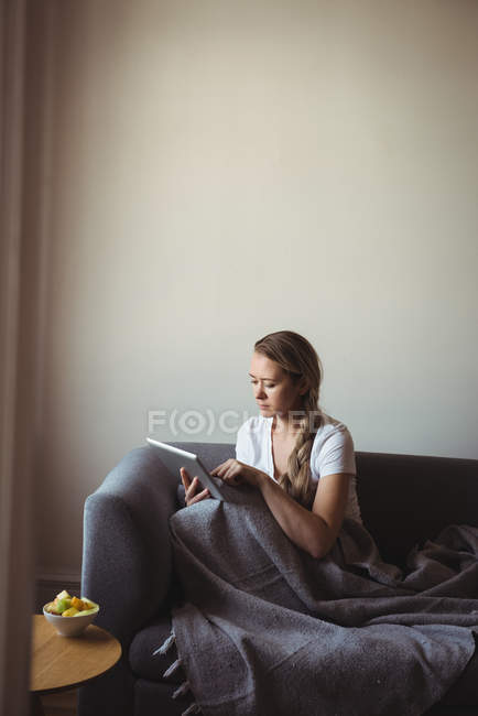 Жінка використовує цифровий планшет, розслабляючись на дивані вдома — стокове фото