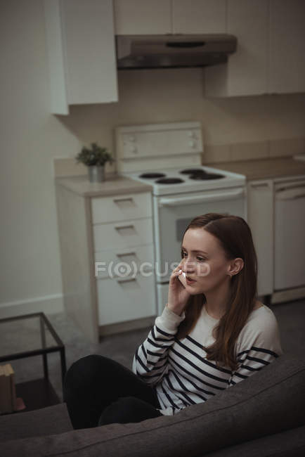 Donna seduta sul divano e che parla sul cellulare a casa — Foto stock
