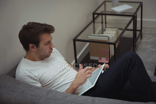 Человек, использующий цифровой планшет на диване дома — стоковое фото