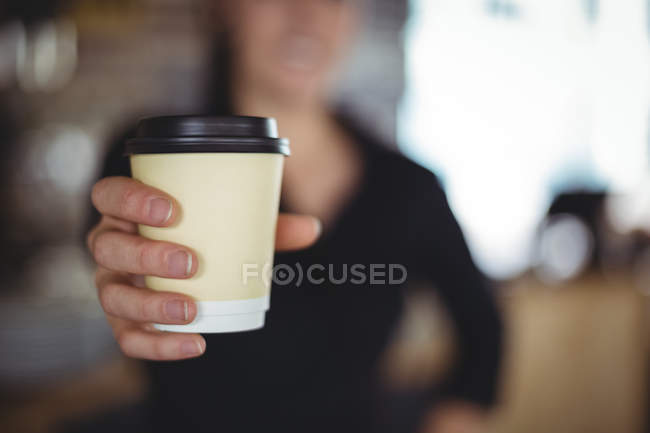 Крупный план официантки, стоящей с одноразовой чашкой кофе в кафе — стоковое фото