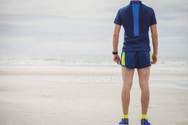 Вид сзади спортсмена, стоящего на песчаном пляже — стоковое фото