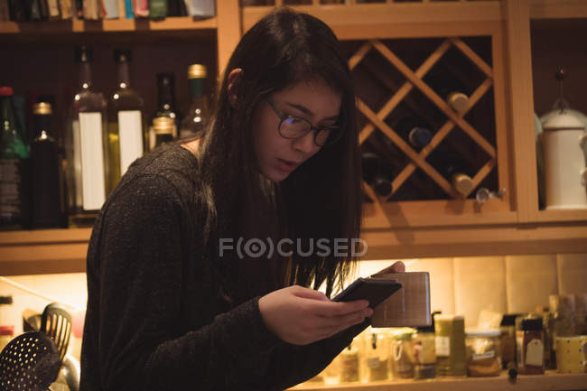 Frau benutzt Handy beim Kaffeetrinken in Küche — Stockfoto