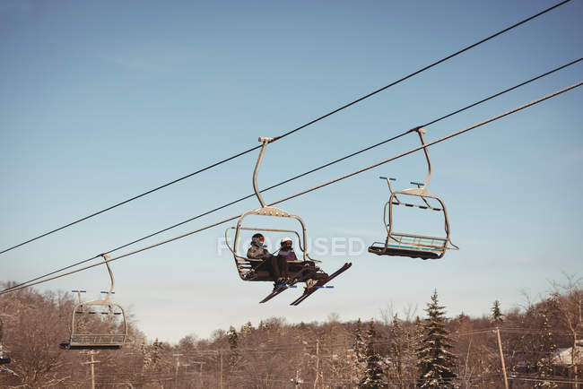 Vista en ángulo bajo de dos esquiadores que viajan en telesilla en la estación de esquí - foto de stock