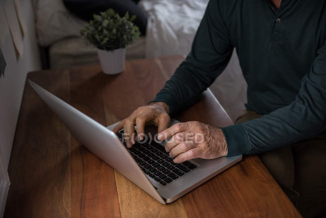Sección media del hombre que utiliza el ordenador portátil en la sala de estar en casa - foto de stock