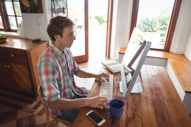 Человек сидит за столом и работает за компьютером дома — стоковое фото