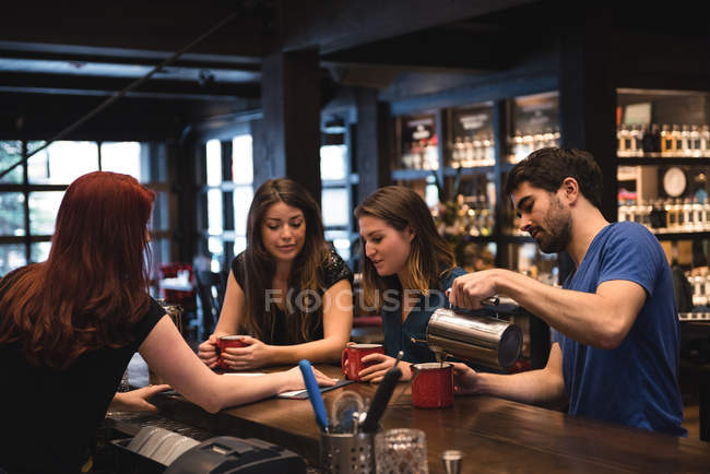 Amis tenant un café au comptoir du bar et interagissant avec le barman — Photo de stock