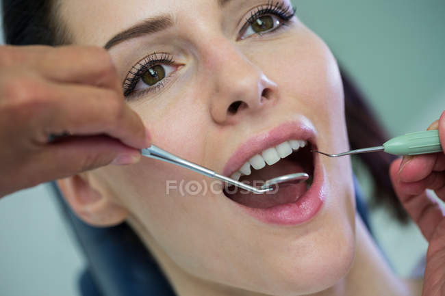 Dentista examinando a una paciente con herramientas en la clínica dental - foto de stock