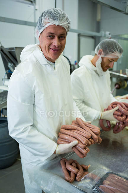 Retrato de carniceros empacando salchichas crudas en fábrica de carne - foto de stock