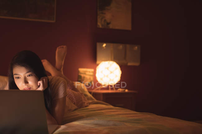 Woman lying and using laptop on bed in bedroom — Stock Photo