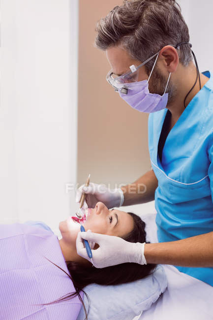 Дантист осматривает пациентку с помощью инструментов в стоматологической клинике — стоковое фото