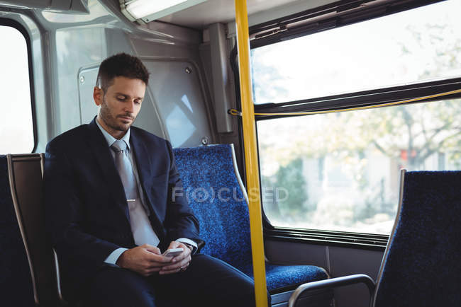 Empresario usando teléfono móvil mientras viaja en el autobús - foto de stock