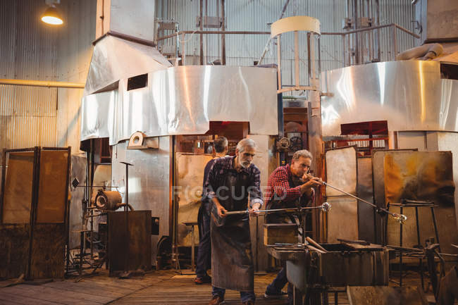 Team of glassblower shaping a glass on the blowpipe at glassblowing factory — Stock Photo