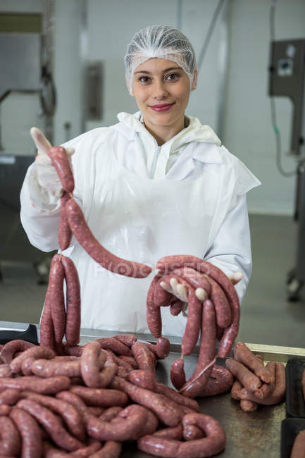 Ritratto di macelleria femminile che tiene salsicce in fabbrica di carne — Foto stock