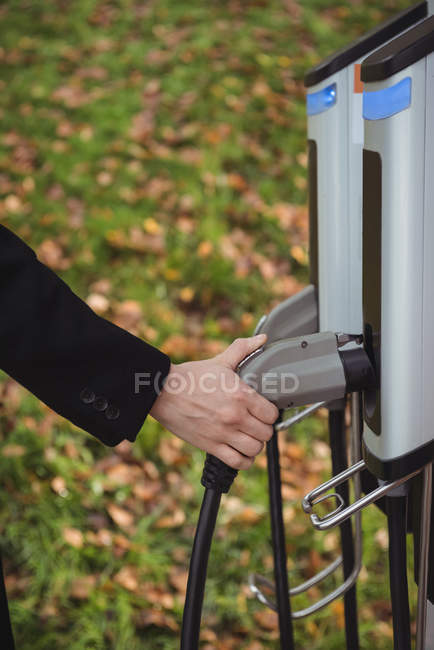Mão de homem segurando carregador de carro na estação de carregamento do veículo elétrico — Fotografia de Stock