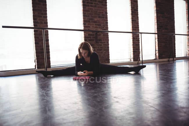 Dançarina alongamento no chão e usando telefone celular no estúdio de dança — Fotografia de Stock