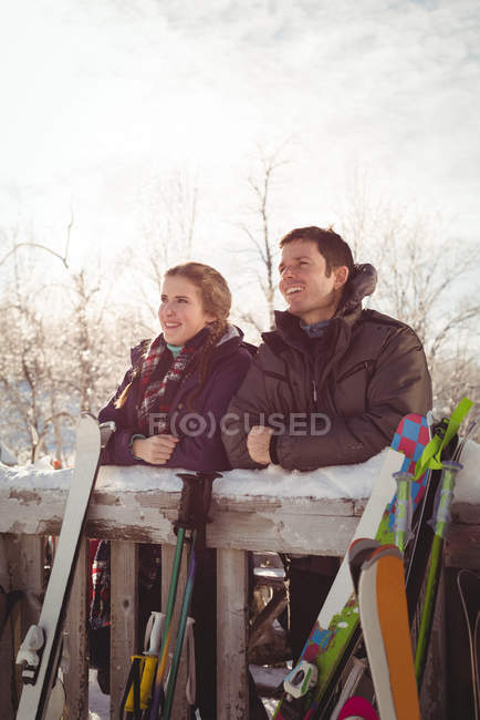 Pareja esquiadora sonriente apoyada en la valla en la estación de esquí - foto de stock