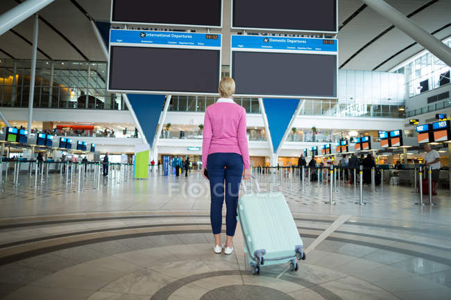 Вид ззаду жіночого комп'ютера, що стоїть з багажем у зоні очікування в аеропорту — стокове фото