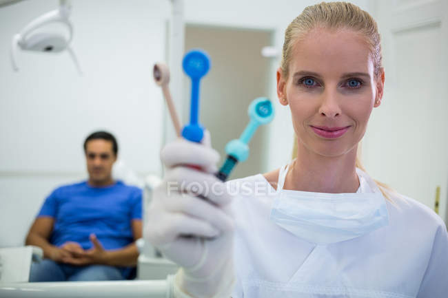 Retrato del dentista sonriente sosteniendo herramientas dentales en la clínica - foto de stock