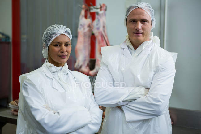Retrato de carniceros de pie con los brazos cruzados en fábrica de carne - foto de stock